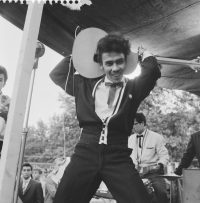 Foto van Oety van Oety & his Real Rockers op het podium in 1960, die zijn gitaar achter zijn hoofd bespeelt.